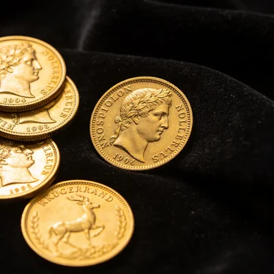 Pièces d'or d'investissement Napoléon et Krugerrand disposées sur un tissu de velours noir foncé, gros plan révélant les gravures et détails de frappe, éclairage doux
