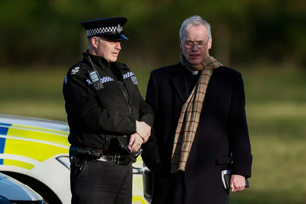 Un policier en uniforme serrant la main d'un civil près d'un véhicule de police.