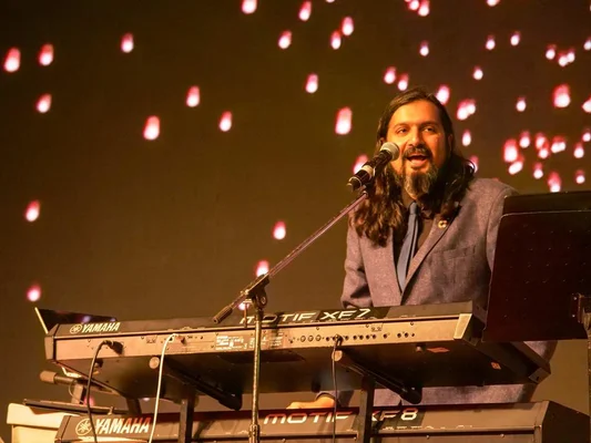 Le musicien Ricky Kej joue du clavier sur une scène éclairée par des lumières rouges et blanches.