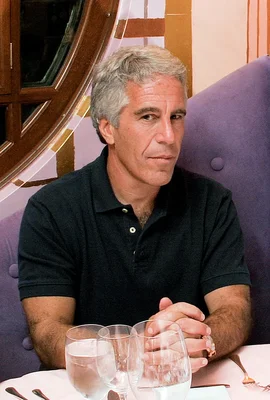 Jeffrey Epstein assis à une table, portant un polo noir.