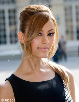 Zahia Dehar photographiée en extérieur, les cheveux blonds relevés en queue de cheval haute.