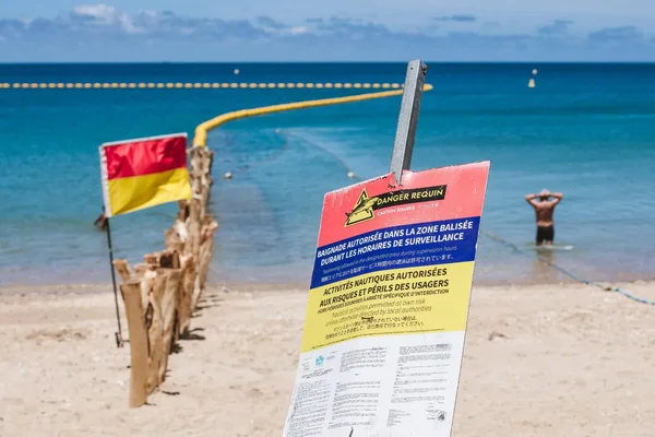 Panneau de signalisation et drapeau avertissant de la présence de requins sur une plage calédonienne.