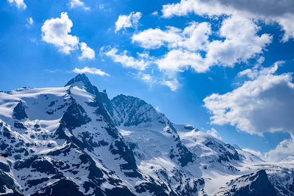 Le Grossglockner en Autriche au printemps, avec ses sommets enneigés sous un ciel bleu nuageux.