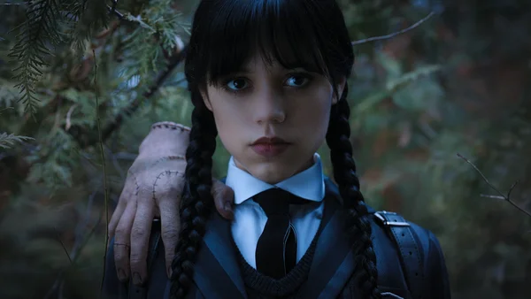 Mercredi Addams en uniforme scolaire avec Thing, la main coupée, dans la forêt.
