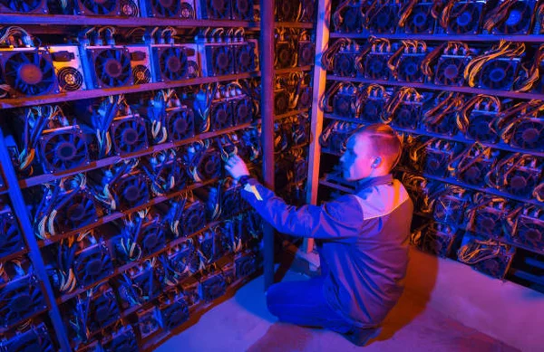 Un technicien en uniforme bleu effectuant la maintenance de serveurs de minage de crypto-monnaies.