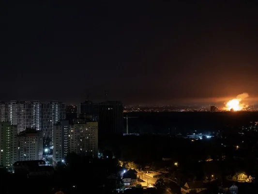 Vue nocturne d'une ville avec des immeubles et un incendie majeur avec des flammes orange à l'horizon