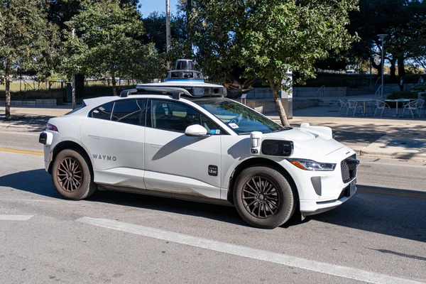 Une voiture autonome Waymo blanche garée dans une rue avec une rangée de capteurs sur le toit.