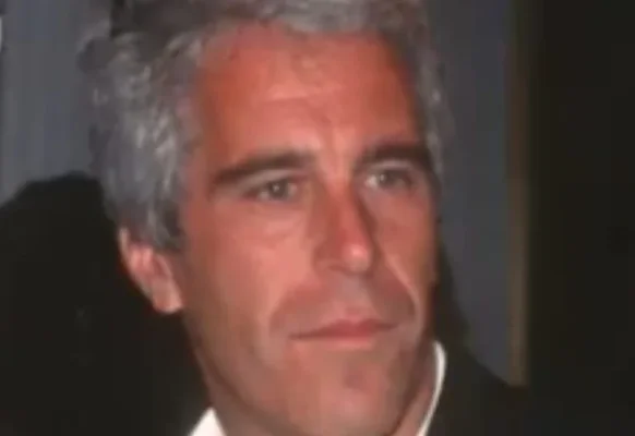 Portrait d'un homme aux cheveux gris portant un costume sombre sur un fond sombre.