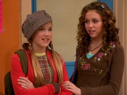 Emily Osment and Miley Cyrus laughing together as Lilly and Miley in Hannah Montana classroom scene