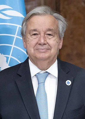 Portrait d'Antonio Guterres, secrétaire général de l'ONU, debout devant un drapeau de l'ONU.