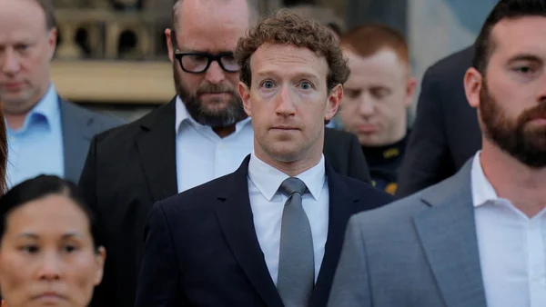 Mark Zuckerberg en costume bleu marine, chemise claire et cravate grise au milieu d'un groupe en tenue formelle