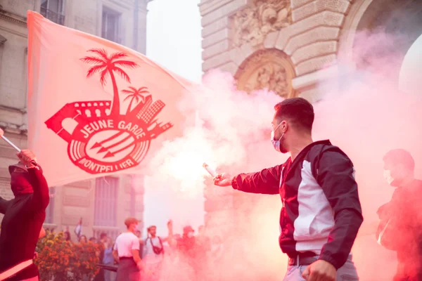 Un homme tient un fumigène devant un grand drapeau de la Jeune Garde Montpellier.