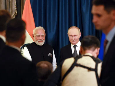 Two men in formal suits posing with an Indian flag in the background