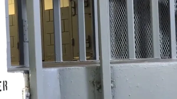 Intérieur d'une cellule de prison avec barreaux métalliques et fenêtre grillagée.