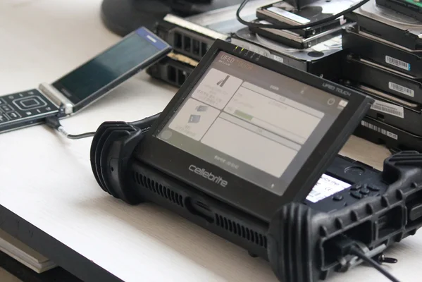 Un appareil Cellebrite UFED Touch visible sur un bureau, accompagné d'un smartphone et d'autres équipements.