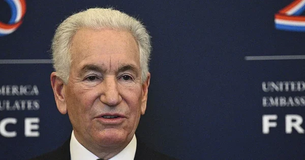 Charles Kushner, ambassadeur américain, devant le logo de l'ambassade des États-Unis.