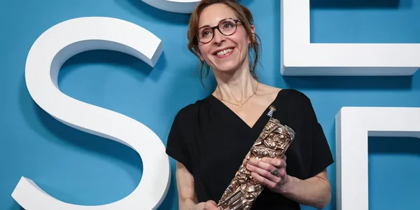 Une femme tenant un trophée devant un fond bleu aux lettres blanches