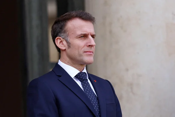 Le président Emmanuel Macron posant devant un mur clair et une porte sombre.