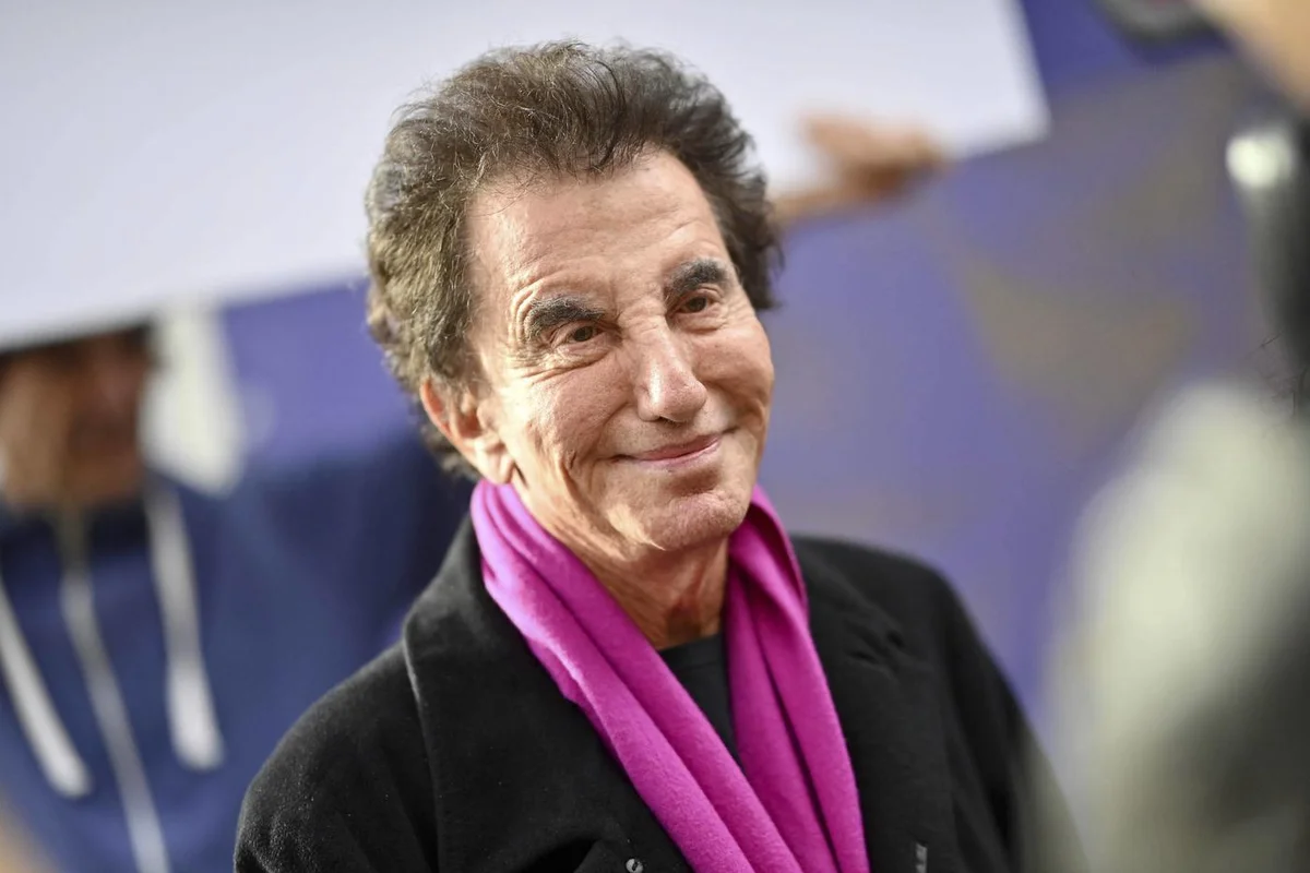 Jack Lang souriant, vêtu d'un manteau noir et d'une écharpe rose.