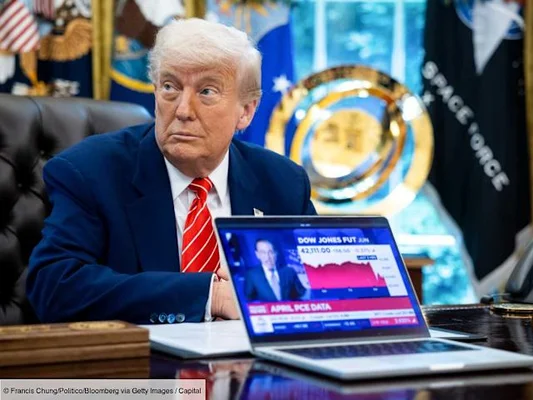 Donald Trump assis à un bureau avec un ordinateur portable affichant un graphique financier.