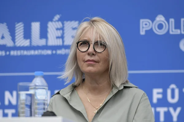 Laurence Fautra, blonde et portant des lunettes, debout devant un fond bleu lors d'une déclaration politique.