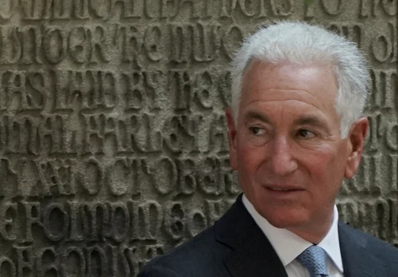 US Ambassador to France Charles Kushner in dark suit and light blue tie standing before stone wall