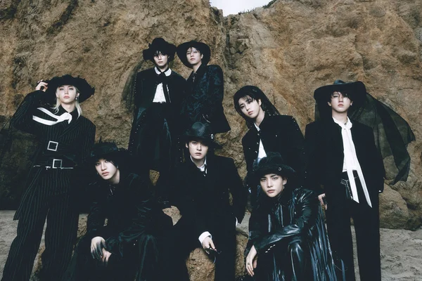 Le groupe Stray Kids pose en tenues sombres devant une falaise rocheuse.