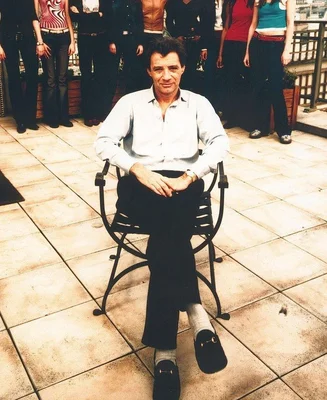 Jean-Luc Brunel assis sur un toit, entouré de plusieurs personnes.