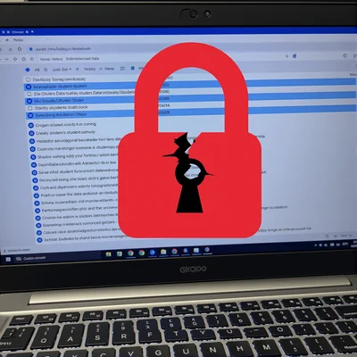 Écran d'ordinateur portable vu de face affichant un dossier scolaire numérique avec des données personnelles visibles, un cadenas rouge brisé en superposition symbolisant la faille de sécurité, éclairage de bureau sombre avec reflets bleutés