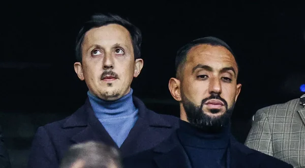 Deux hommes en costume et col roulé sombre, barbus, posent côte à côte.