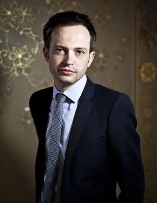 Pierre-Yves Bournazel en costume et chemise bleue sur fond marron.