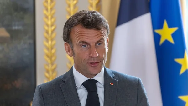 Emmanuel Macron en costume, debout dans un cadre officiel devant les drapeaux français et européen.