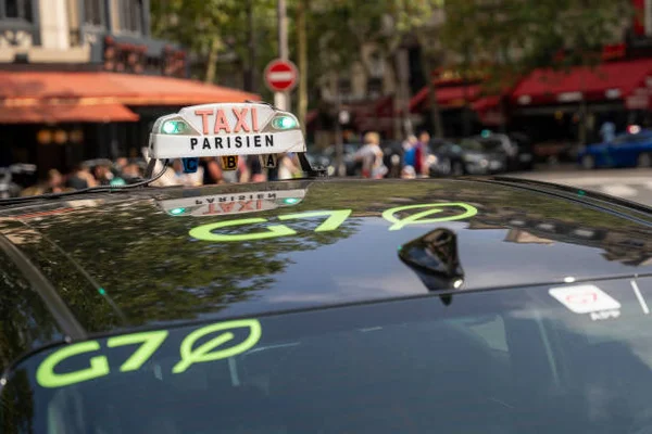 Flotte de taxis G7 circulant sur une avenue parisienne avec l'Arc de Triomphe en arrière-plan