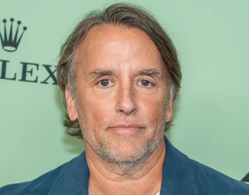 Un homme aux cheveux mi-longs portant une veste bleue sur fond vert