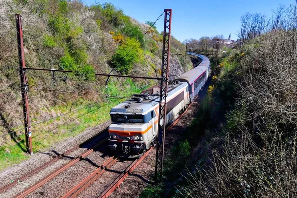 Locomotive grise et orange tirant des voitures de voyageurs dans la campagne