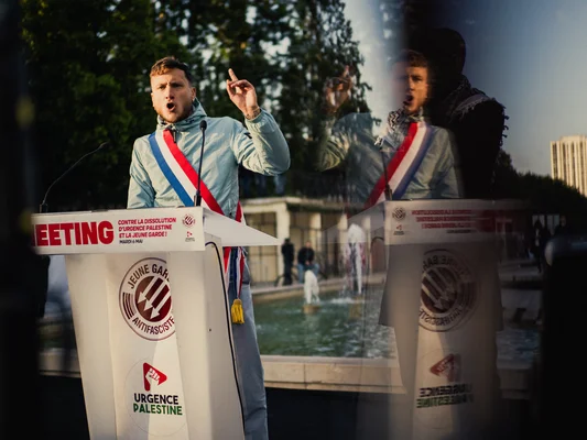 Un homme s'exprime devant une banderole Jeune Garde antifasciste et Urgence Palestine.