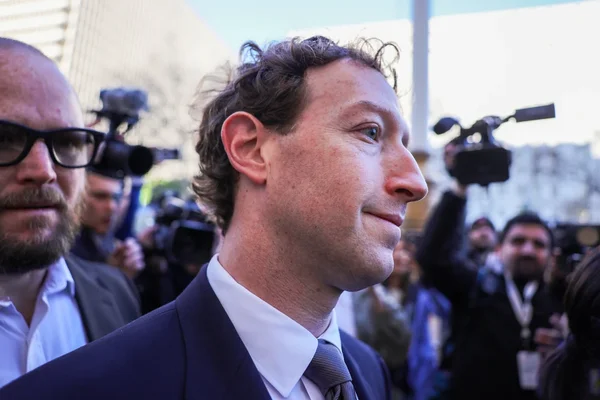 Mark Zuckerberg en costume et cravate grise à l'extérieur, entouré de personnes et de matériel médiatique