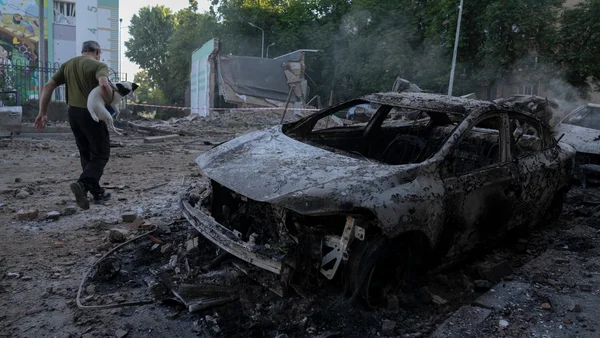 Un résident ukrainien s'éloignant avec son chien blanc près d'un véhicule calciné dans une zone dévastée par les attaques