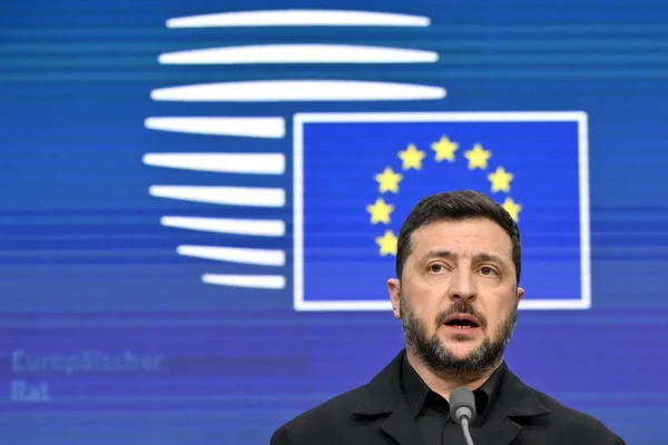 Un homme en costume s'exprime au micro devant le drapeau de l'Union européenne.