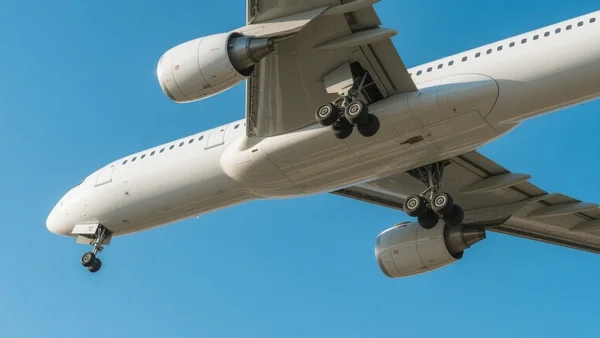 Vue au sol d'un avion de ligne moderne au soleil, train d'atterrissage visible, fond de ciel bleu dégagé