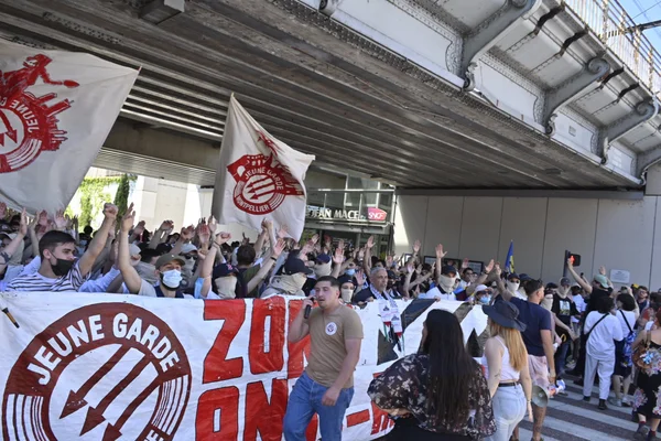 Rassemblement de soutien à la Jeune Garde sous un pont avec des drapeaux blancs et rouges.