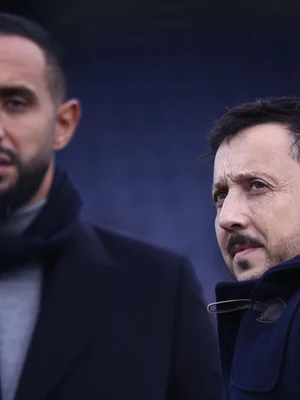 Deux hommes en manteaux foncés, l'un au premier plan regardant vers le haut.