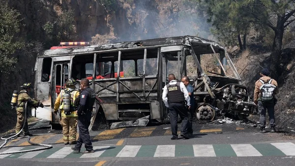 Les restes d'un bus brûlé sur une route, examinés par les secours.
