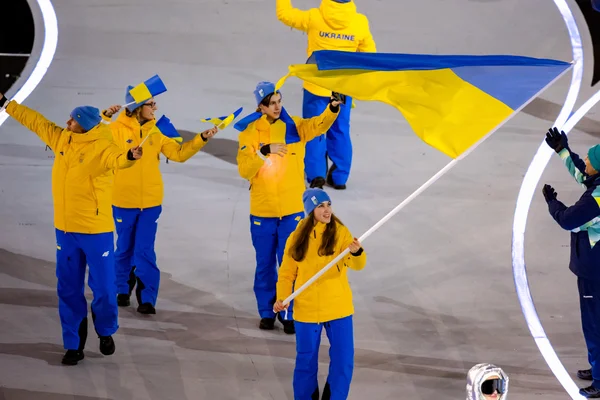 Des athlètes ukrainiens en tenue jaune et bleue défilent lors d'une cérémonie, portant un drapeau national.