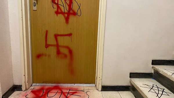 A resident points to hateful graffiti tags spray-painted on a residential building door or wall.