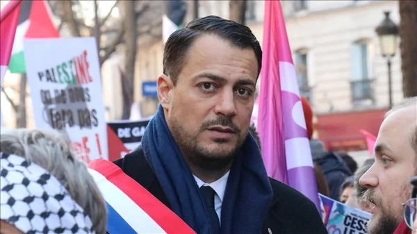 Homme en manteau sombre lors d'un rassemblement public avec drapeaux et pancartes à Marseille.