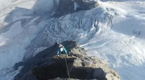Un alpiniste grimpe sur un rocher avec un glacier en toile de fond.