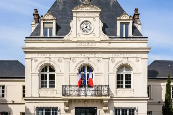 Façade d'une mairie française arborant la devise nationale et les drapeaux français et européen sur un balcon.