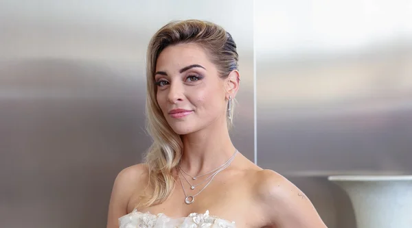 Priscilla Betti posant en robe blanche ornée de dentelles et de bijoux.