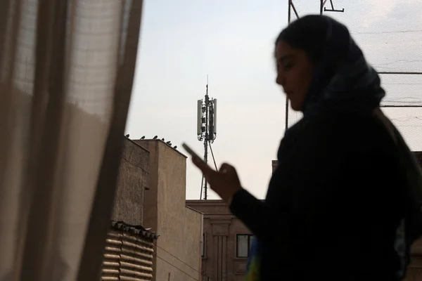 Personne tenant un smartphone avec une antenne relais en arrière-plan en Iran.
